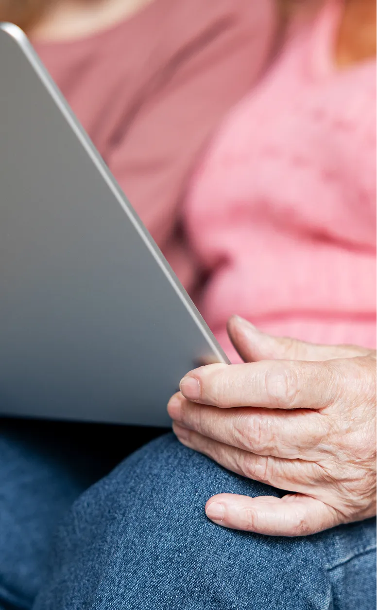 Eine ältere Person hält ein Tablet, während sie mit einer Begleitperson spricht, die Unterstützung bei Pflegeberatung bietet.